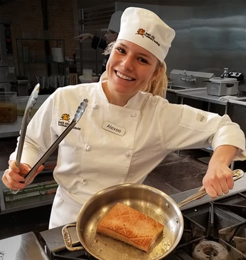 Park City Culinary Institute student Alexee cooking a fish and smiling.