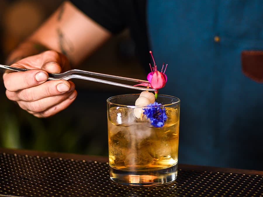 Photo of somebody garnishing a cocktail with edible flowers.