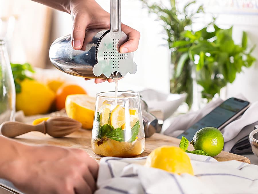Photo of somebody pouring a cocktail shaker into a glass filled with mint and citrus.