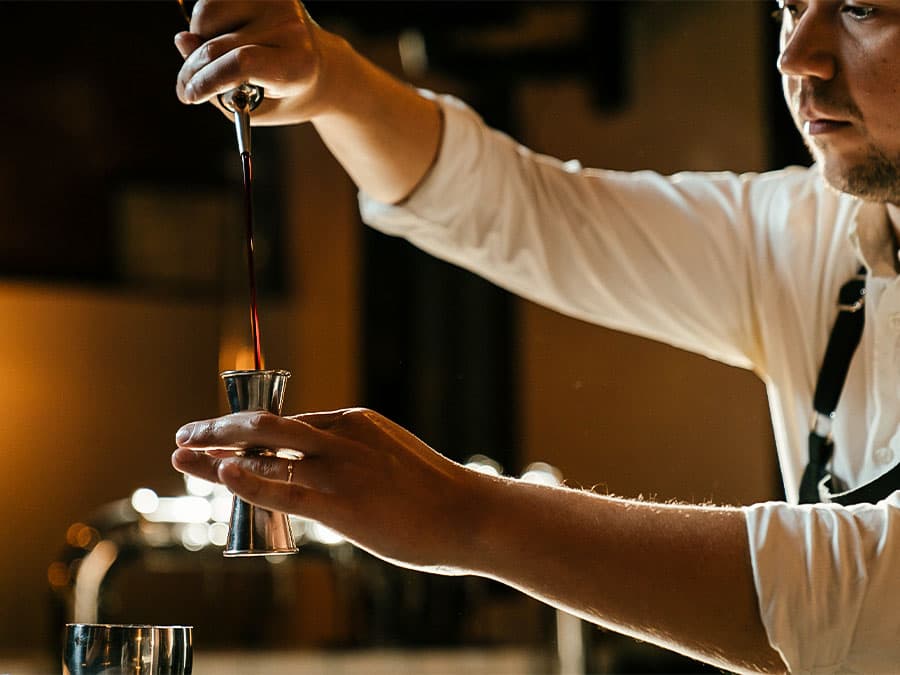 Photo of a bartender pouring a liqueur into jigger.