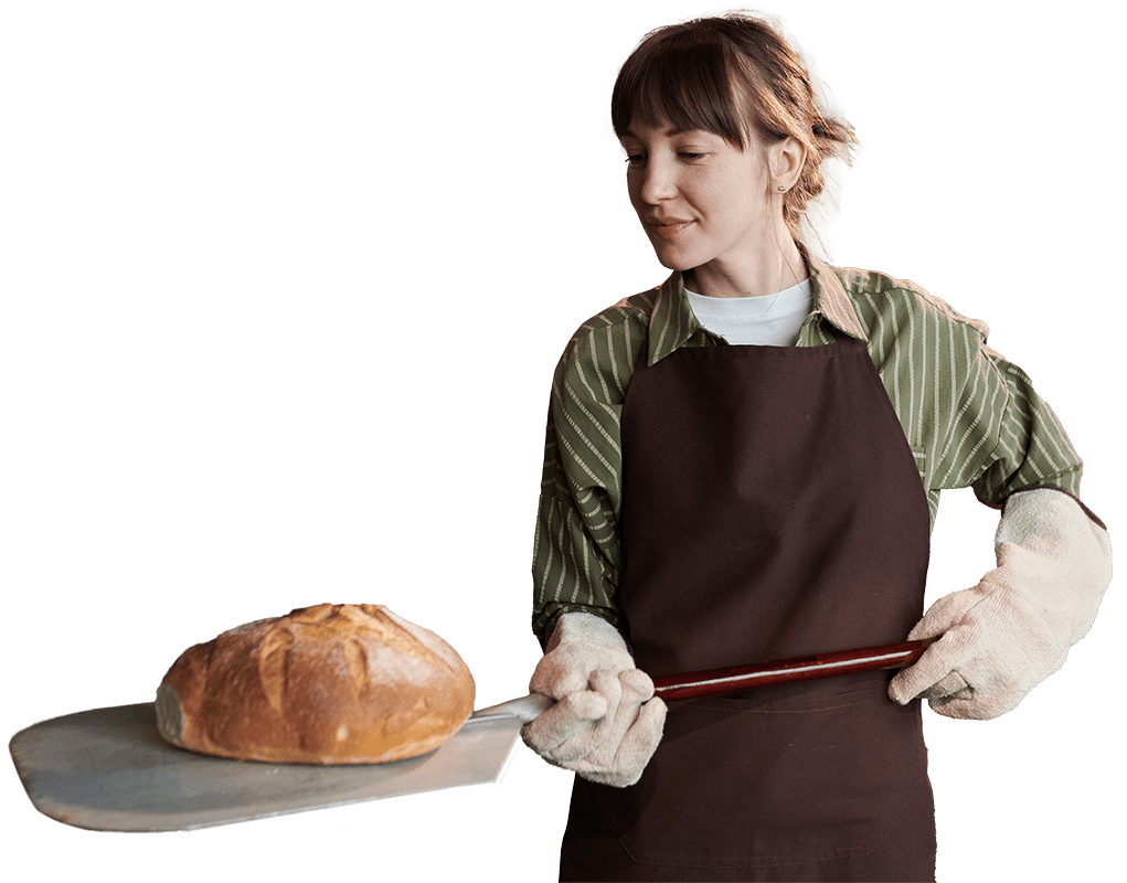 Baker pulling a fresh loaf of sourdough bread out of the oven